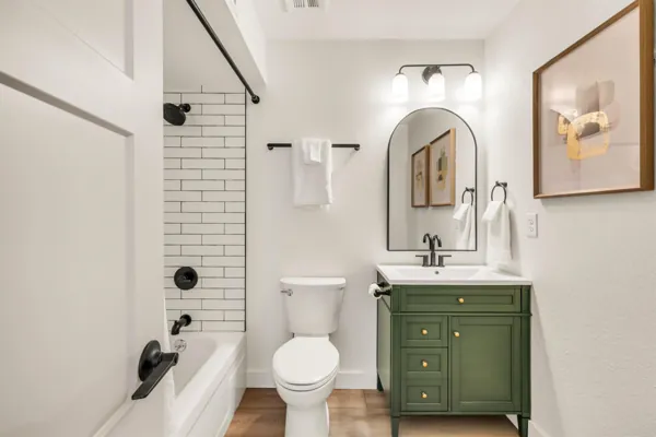 This modern bathroom in Mesa, AZ features a green vanity, white tub with black fixtures, and stylish decor, captured with expert real estate photography.