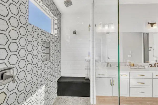 This modern bathroom in Phoenix, AZ features a stylish shower with hexagonal and subway tiles, a built-in bench, and a white vanity, captured in professional real estate photography.
