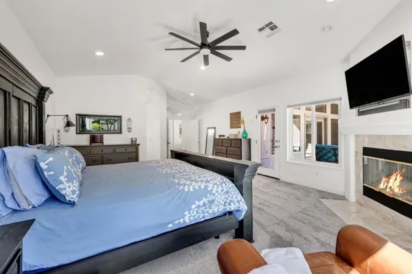 This spacious master bedroom in Gilbert, AZ features a cozy fireplace, flat screen TV, and modern furnishings, captured through expert real estate photography to highlight its comfortable design.