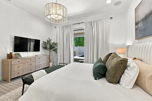 This real estate photography showcases a modern bedroom in Mesa, AZ, featuring elegant lighting, a large TV, and stylish decor, making it an attractive property prospect.