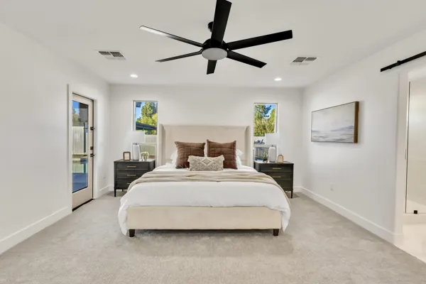 This modern bedroom in Phoenix, AZ features a large bed, ceiling fan, and neutral decor, captured through professional real estate photography highlighting the room's comfort and style.