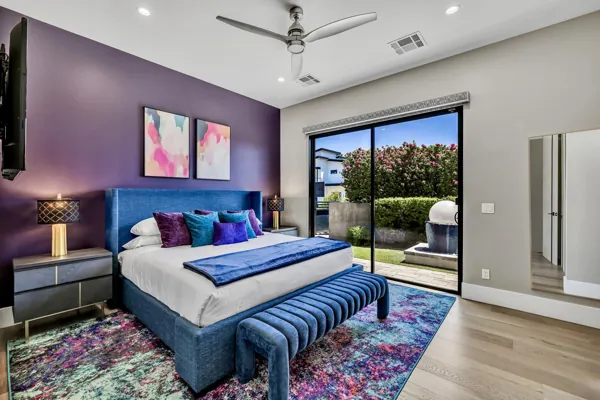 This modern bedroom features a purple accent wall, vibrant decor, and sliding glass doors opening to a lush garden, captured in expert real estate photography in Scottsdale, AZ.