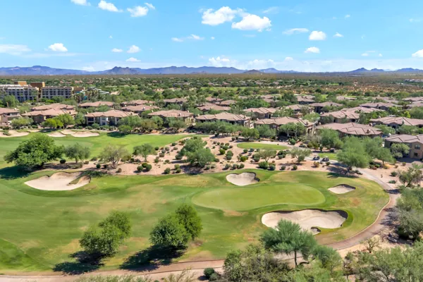 This aerial real estate photography features a scenic golf course community in Phoenix, AZ, showcasing homes nestled near lush greens and desert landscape with mountains in the background.