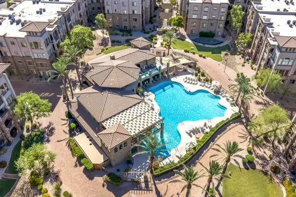 Aerial real estate photography of a residential complex in Phoenix, AZ featuring a large swimming pool, lounge chairs, and surrounding landscaped grounds and buildings.