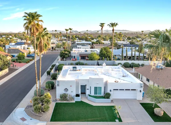 This aerial real estate photography showcases a charming suburban home with desert landscaping and palm trees in Scottsdale, AZ, highlighting the quiet neighborhood and scenic mountain views.