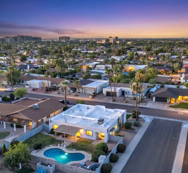 This stunning aerial real estate photography showcases a Scottsdale, AZ neighborhood at dusk, highlighting homes with lush landscaping and a beautiful backyard pool.