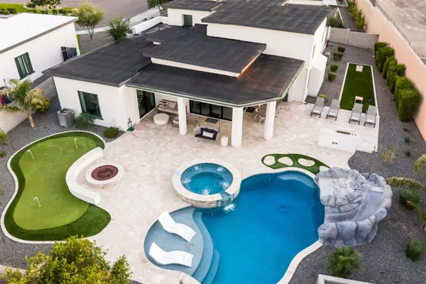 Stunning aerial view of a Scottsdale, AZ backyard featuring a pool, hot tub, putting green, and spacious patio captured with expert real estate photography.