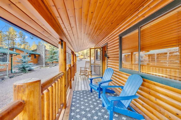 Cozy log cabin porch in Greer, AZ featuring blue Adirondack chairs and wooden railing captured with professional real estate photography showcasing rustic charm.