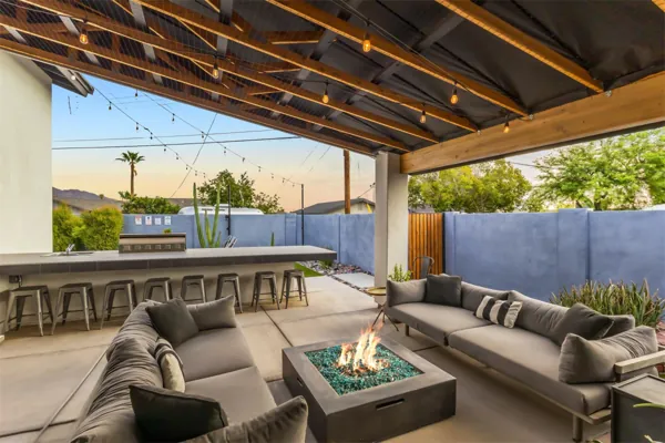 This stylish covered backyard patio in Scottsdale, AZ features a fire pit, outdoor kitchen, and ample seating, captured with professional real estate photography to highlight its inviting atmosphere.