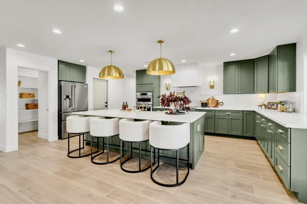 This kitchen in Phoenix, AZ features modern green cabinetry, a spacious island with gold pendant lights, and sleek appliances, captured with professional real estate photography to showcase the stylish design.