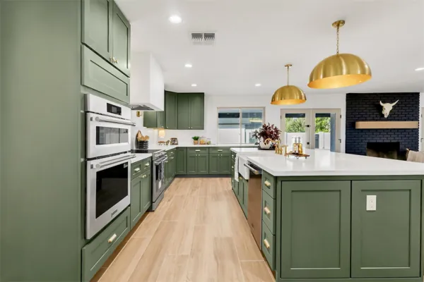 This modern kitchen in Phoenix, AZ features green cabinetry, gold light fixtures, and stainless steel appliances, beautifully captured through professional real estate photography.