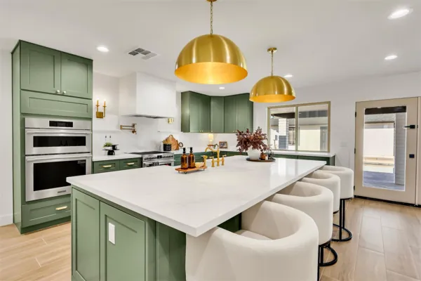 This modern kitchen in Phoenix, AZ features green cabinetry, gold pendant lights, and a large white island, captured beautifully through expert real estate photography.