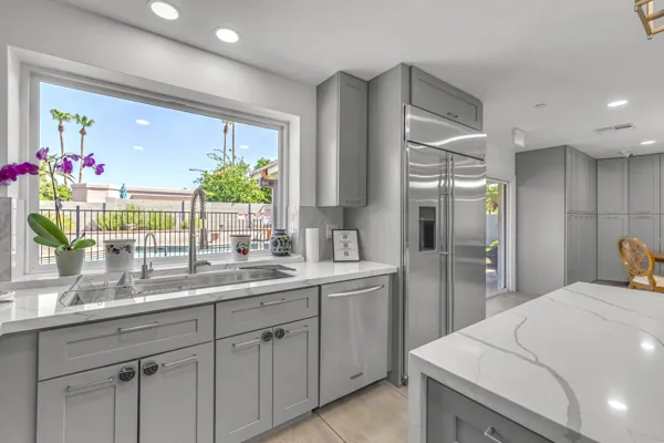 This modern kitchen in Scottsdale, AZ features sleek gray cabinetry, a large window with a pool view, and stainless steel appliances, captured with professional real estate photography.