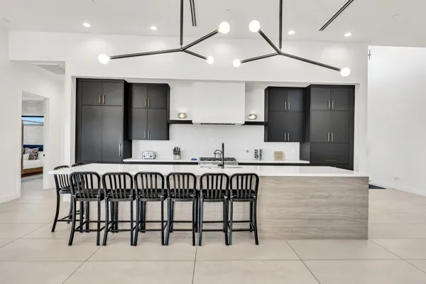 This modern kitchen in Scottsdale, AZ features sleek black cabinets, a large island with barstools, and contemporary lighting, captured with professional real estate photography.