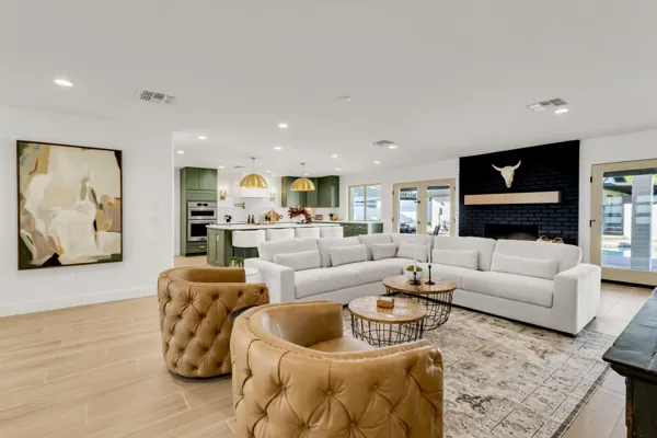 This modern open-concept living room and kitchen in Phoenix, AZ, features stylish green cabinetry, leather chairs, and bright natural lighting, captured expertly with real estate photography.