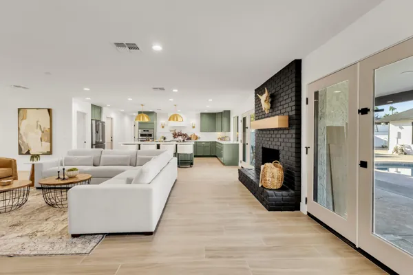 This modern open floor plan features a spacious living room and kitchen with green cabinetry and a black brick fireplace, showcasing stylish real estate photography in Phoenix, AZ.
