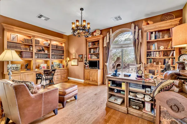 This Scottsdale, AZ home office features warm wood bookshelves, leather furniture, and a large arched window, captured with expert real estate photography to highlight its inviting ambiance.