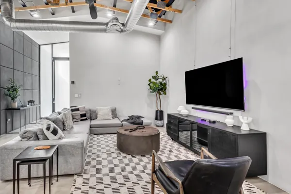 This modern living room in Scottsdale, AZ, features a spacious grey sectional sofa, large TV setup, and industrial ceiling details, captured with high-quality real estate photography.