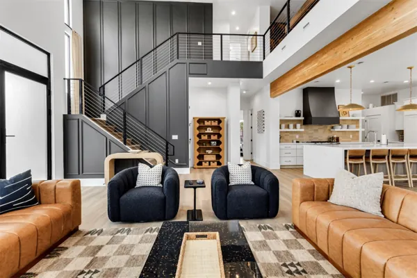 This modern living room in Scottsdale, AZ features stylish seating, a staircase with metal railing, and an open kitchen, captured with professional real estate photography highlighting spacious design.