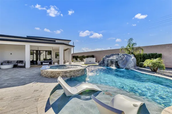 This Scottsdale, AZ backyard features a luxurious pool with a waterfall, spa, and poolside lounge chairs, captured with professional real estate photography to highlight its inviting outdoor living space.