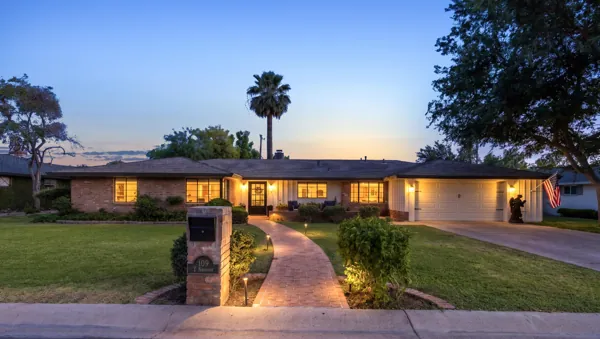 This twilight real estate photography showcases a charming brick home with an inviting lit pathway and garage in Phoenix, AZ, highlighting its warm and welcoming exterior ambiance.