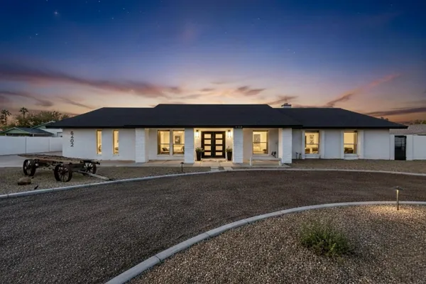 Captivating twilight exterior view of a modern house featuring a circular driveway and warm interior lighting, showcasing stunning real estate photography in Phoenix, AZ.