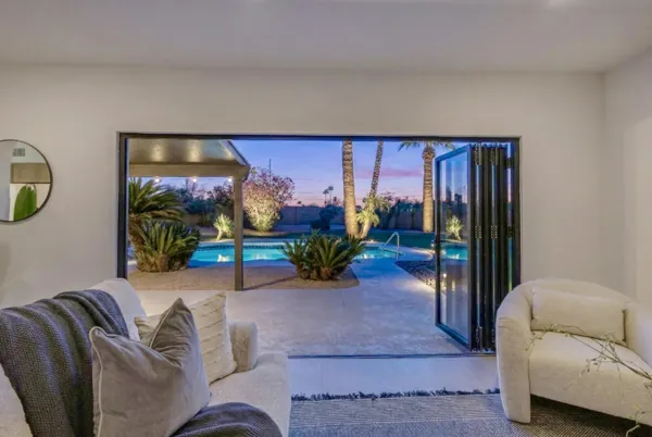 This Scottsdale, AZ home features a spacious living room with open folding doors leading to a beautifully lit backyard pool area, captured with expert real estate photography.